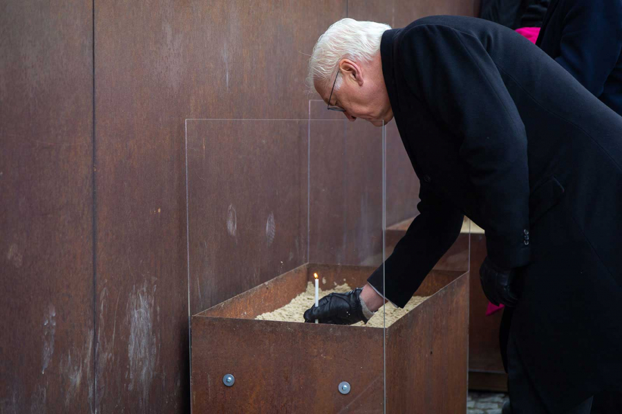 Frank-Walter Steinmeier steht am Denkmal der Gedenkstätte Berliner Mauer und beugt sich zu einer entzündeten Kerze in einem Sandbecken hinunter.